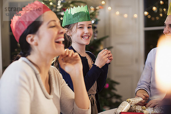 Glückliche Familie in Papierkronen lacht beim Weihnachtsessen