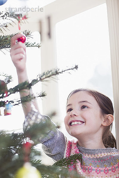 Lächelndes  neugieriges Mädchen  das ein Ornament am Weihnachtsbaum berührt