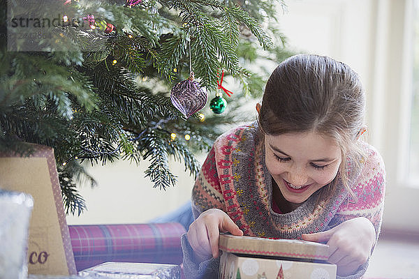 Lächelndes  neugieriges Mädchen öffnet Weihnachtsgeschenk