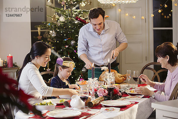 Mehrgenerationen-Familie tranchiert Weihnachtstruthahn bei Kerzenlicht am Tisch