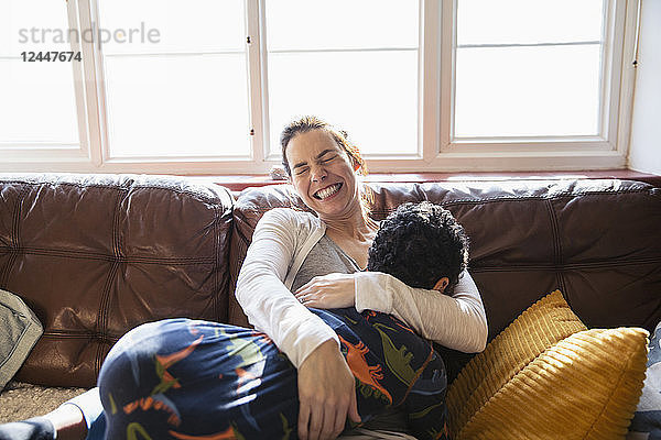Glückliche  sorglose Mutter kuschelt mit ihrem Sohn auf dem Wohnzimmersofa