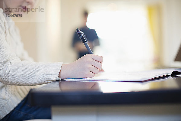 Mädchen mit Stift und Arbeitsheft bei den Hausaufgaben am Tisch