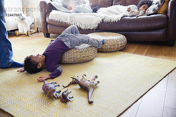 Verspielter Junge mit Dinosaurier-Spielzeug auf dem Boden im Wohnzimmer