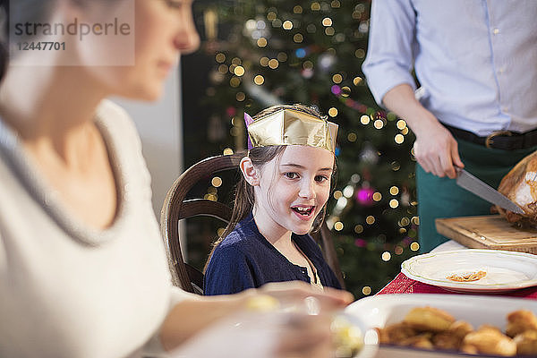 Lächelndes Mädchen mit Papierkrone beim Weihnachtsessen