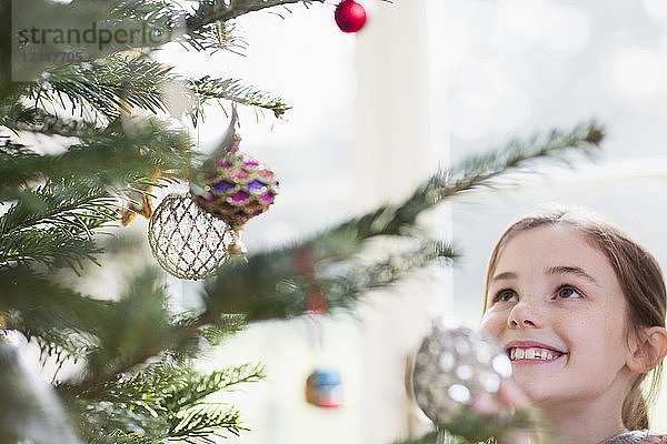 Lächelndes Mädchen mit Blick auf den Schmuck am Weihnachtsbaum