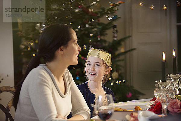 Glückliche Mutter und Tochter in Papierkrone bei Kerzenschein Weihnachtsessen Tisch