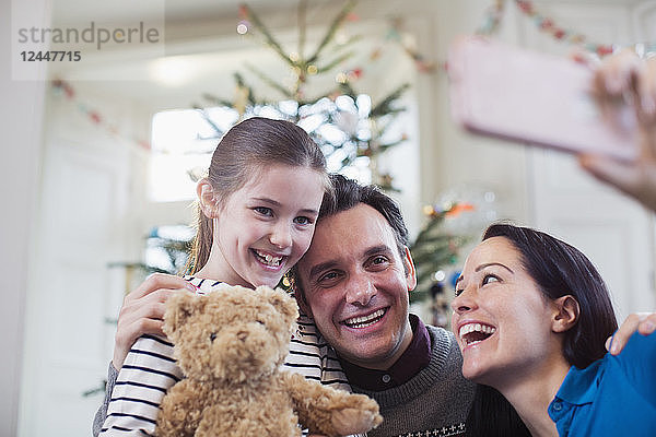 Glückliche Eltern und Tochter machen ein Selfie vor dem Weihnachtsbaum