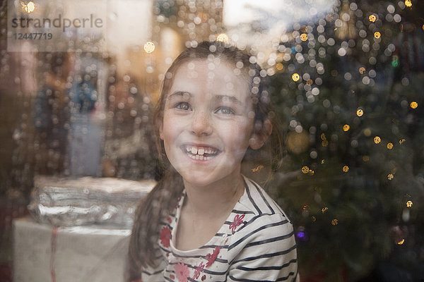 Porträt glückliches Mädchen an nassem Fenster im Weihnachtswohnzimmer