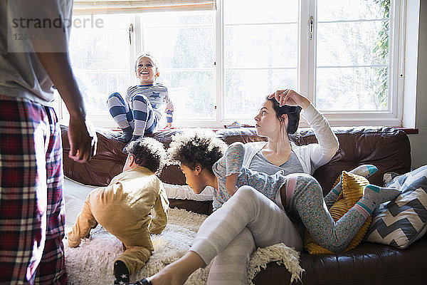 Multiethnische junge Familie im Schlafanzug spielt im sonnigen Wohnzimmer