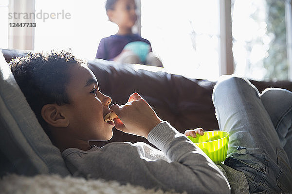 Junge isst Snack und sieht auf dem Sofa fern