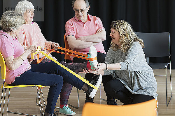 Instructor helping active seniors stretching legs  exercising with straps