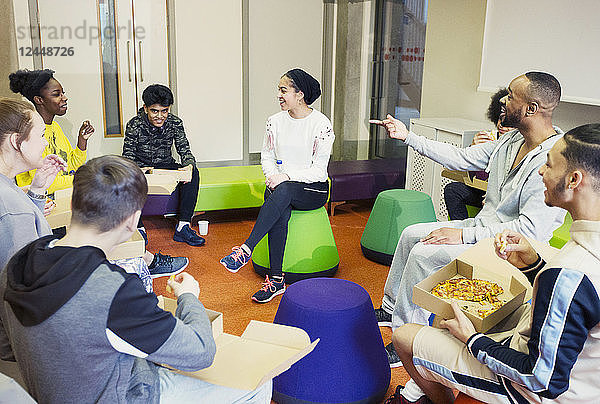 Teenagers and mentor talking and eating pizza in community center