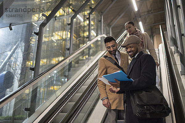 Businessmen discussing paperwork on urban escalator at night