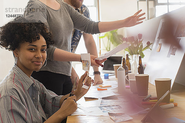 Portrait confident creative designer cutting photographs in office