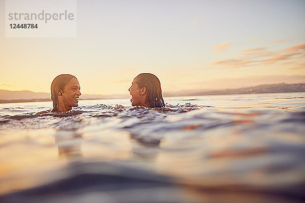 Young couple swimming in ocean at sunset