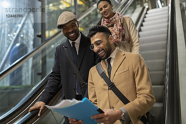 Smiling business people reading paperwork on escalator