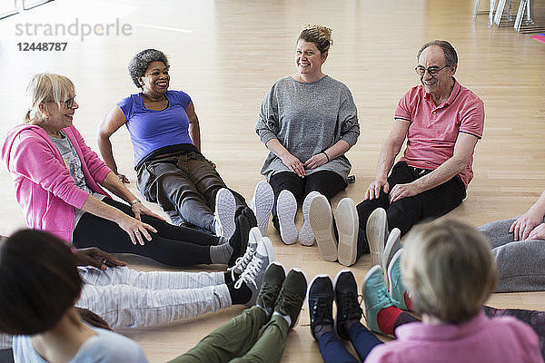 Instructor and active seniors stretching legs in circle in exercise class