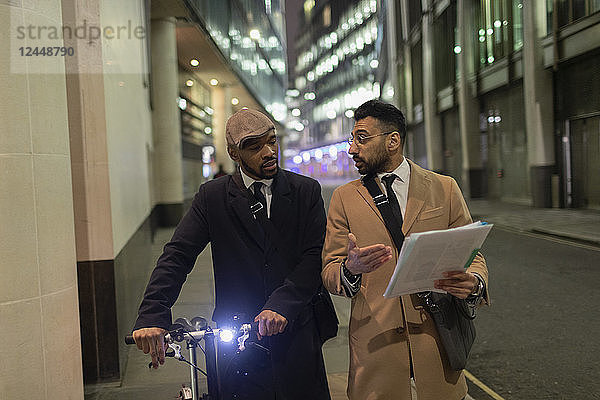 Businessmen with bicycle and paperwork walking on urban sidewalk