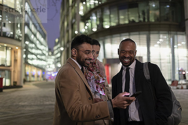 Business people using smart phone on urban street at night