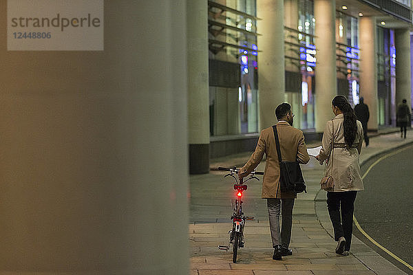 Business people with bicycle walking on urban sidewalk at night