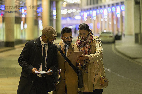 Business people using digital tablet on urban street at night