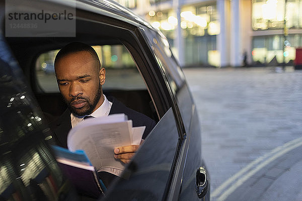 Businessman reading paperwork in crowdsourced taxi at night