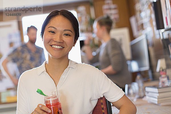 Portrait smiling creative businesswoman drinking juice in office