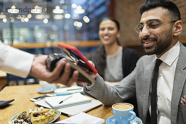 Businessman paying with smart phone contactless payment in cafe