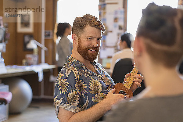Smiling creative businessman playing ukulele in office