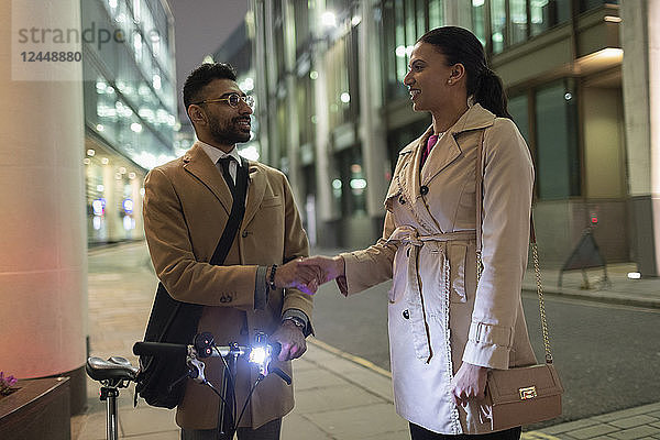 Business people with bicycle handshaking on urban sidewalk at night