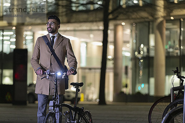 Businessman with bicycle on urban street at night