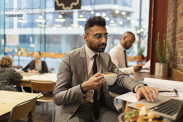 Focused businessman drinking coffee and working at laptop in cafe