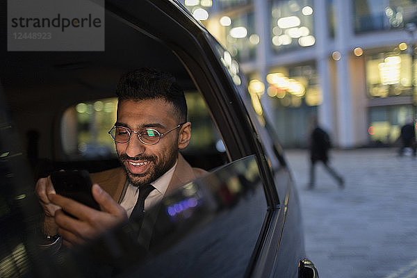 Businessman using smart phone in crowdsourced taxi at night