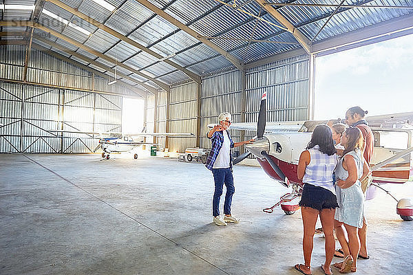 Pilot talking to friends at prop airplane in airplane hangar
