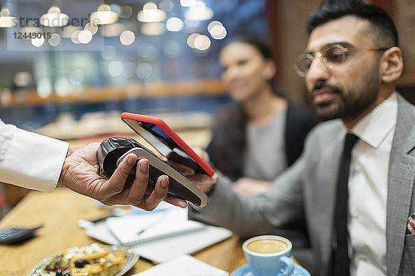 Businessman in cafe paying with smart phone contactless payment