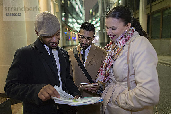 Business people reviewing paperwork on urban sidewalk at night