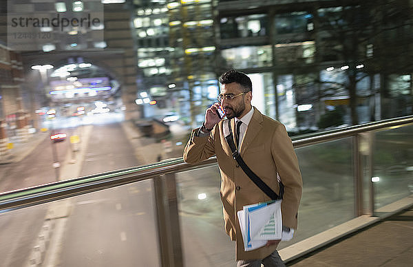 Businessman talking on smart phone  walking on urban pedestrian bridge at night
