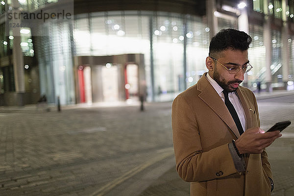 Businessman texting with smart phone on urban street corner at night