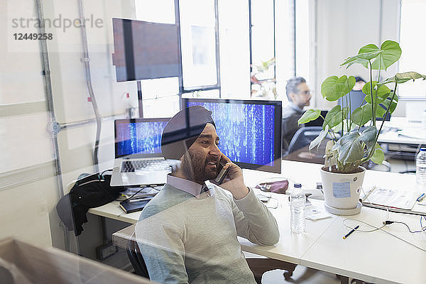Indian computer programmer in turban talking on smart phone in office