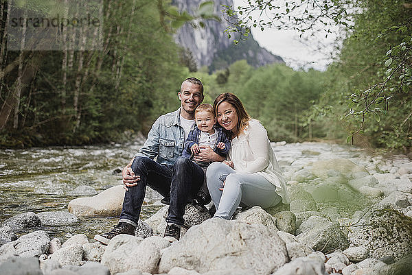 Portrait parents and baby son sitting on rocks at riverside