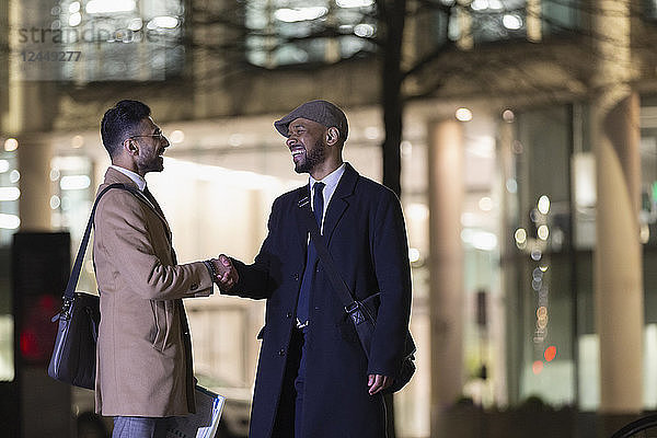 Businessmen handshaking on urban street at night