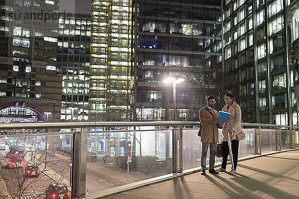 Business people discussing paperwork on urban pedestrian bridge at night