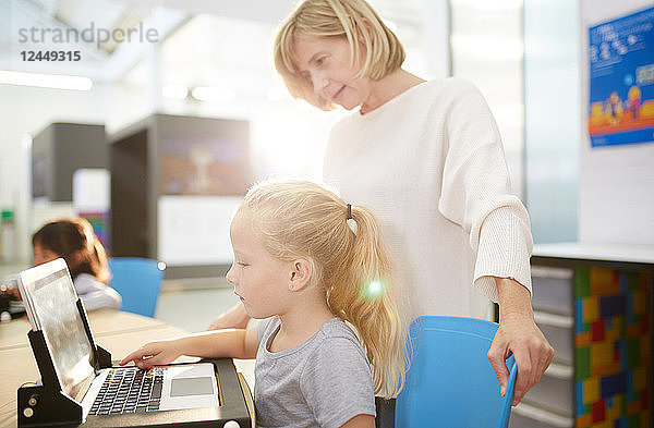 Teacher and schoolgirl using laptop in science center