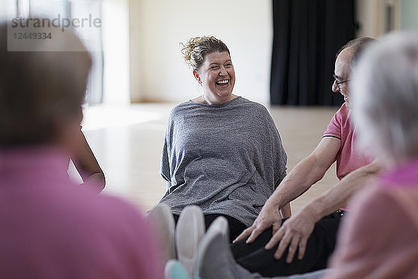 Laughing instructor and active seniors stretching legs in exercise class