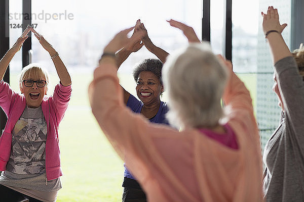 Happy active senior women exercising  stretching arms overhead in exercise class