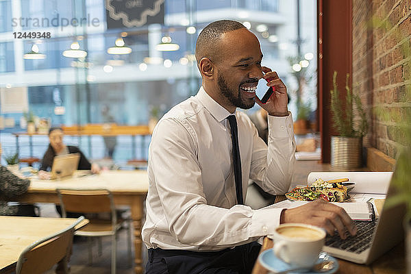 Smiling businessman talking on smart phone  working in cafe