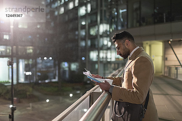 Businessman reviewing paperwork on urban pedestrian bridge at night