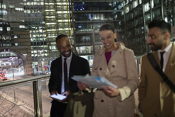 Business people reviewing paperwork on urban pedestrian bridge at night
