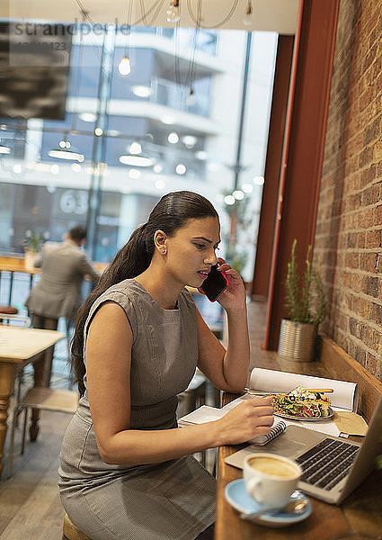 Businesswoman talking on smart phone  working at laptop in cafe