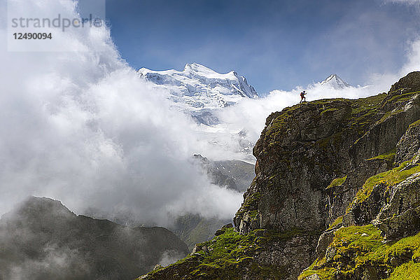 Wanderer auf steilem Grat mit Bergkette im Hintergrund